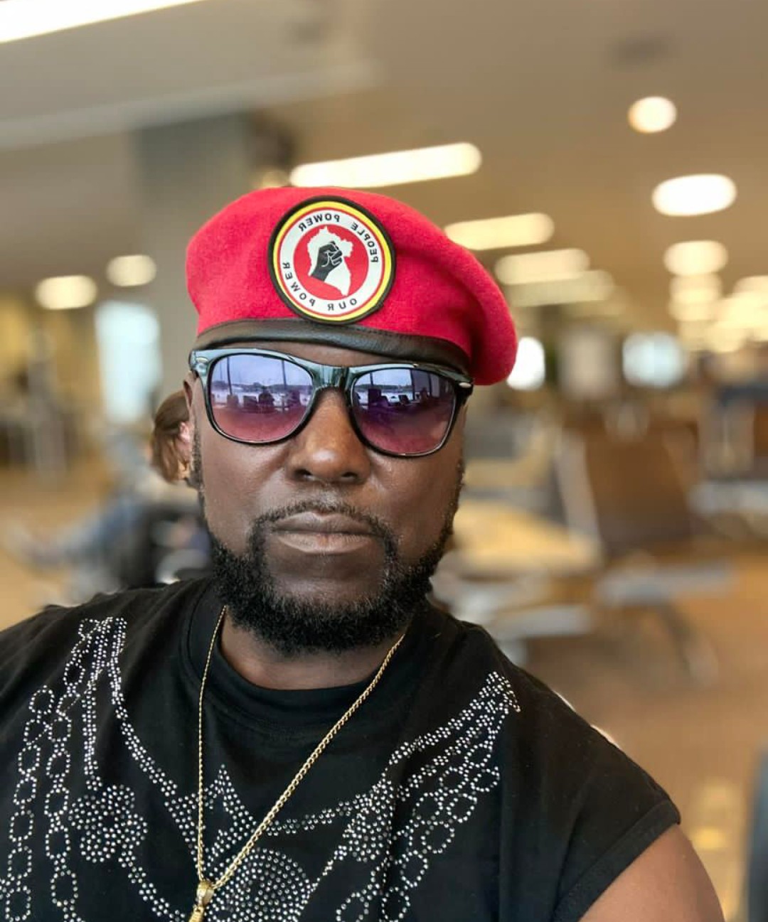 Photograph of DJ Bernazo in a black and white detailed shirt, gold necklace, sunglasses, and red hat with blurred background | Black Owned Maine Portland