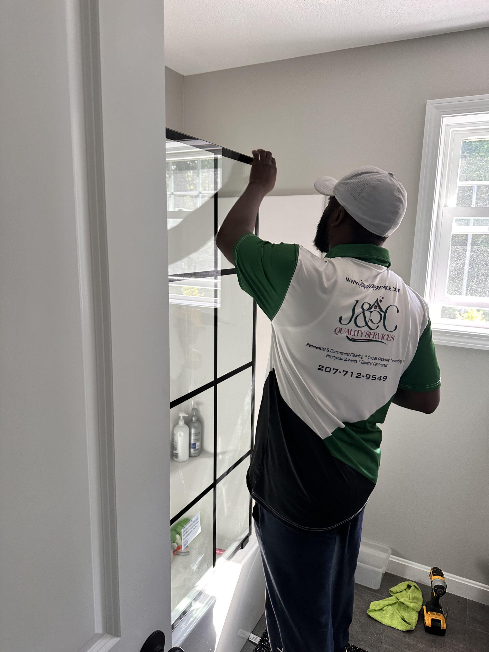 Photo of man installing a shower door - black paned glass door in a white bathroom | Black Owned Maine Portland