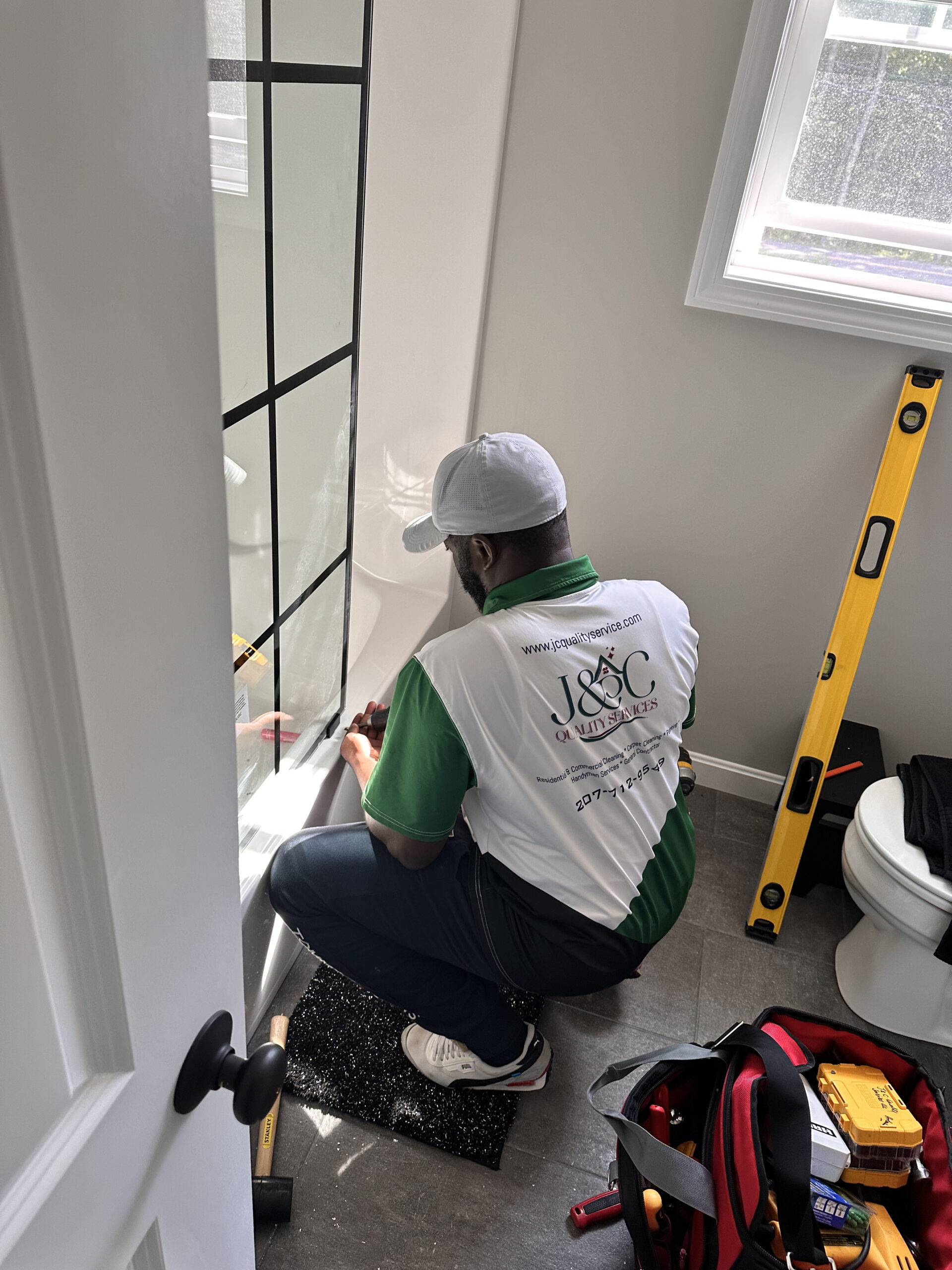 Photo of J&C Quality Services installing a shower door in a white bathroom | Black Owned Maine Portland